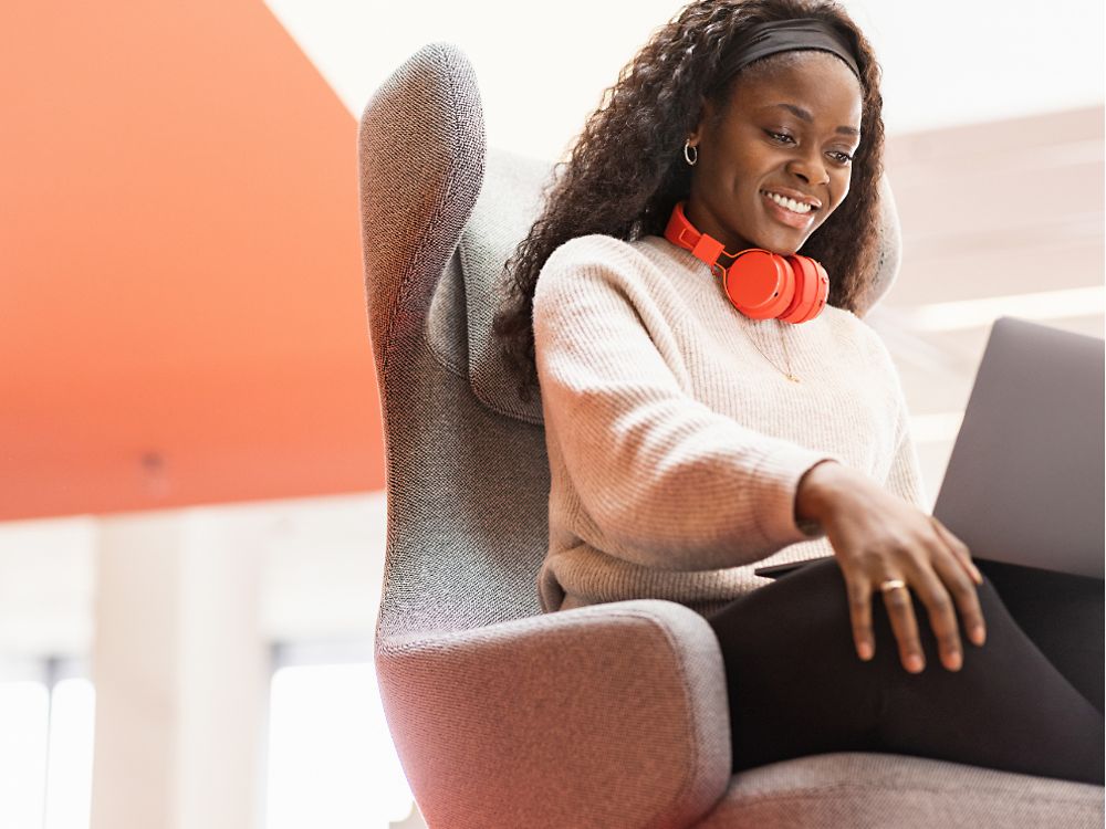 En Henkel-anställd sitter i en bekväm stol med sin bärbara dator på knäna. Hon ler. 