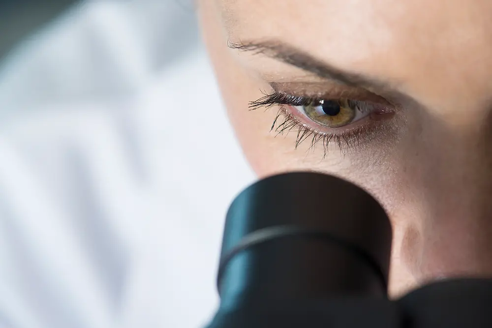 En kvinnas öga tittar genom ett mikroskop