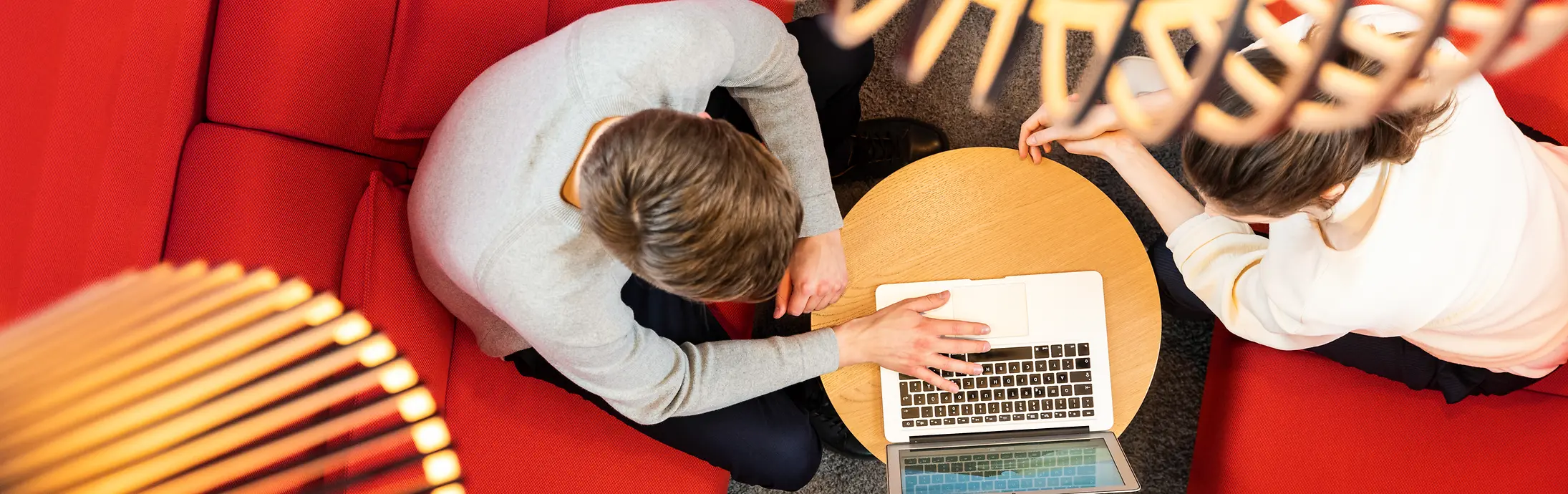 Två personer sitter på en röd soffa och arbetar tillsammans på en dator. 
