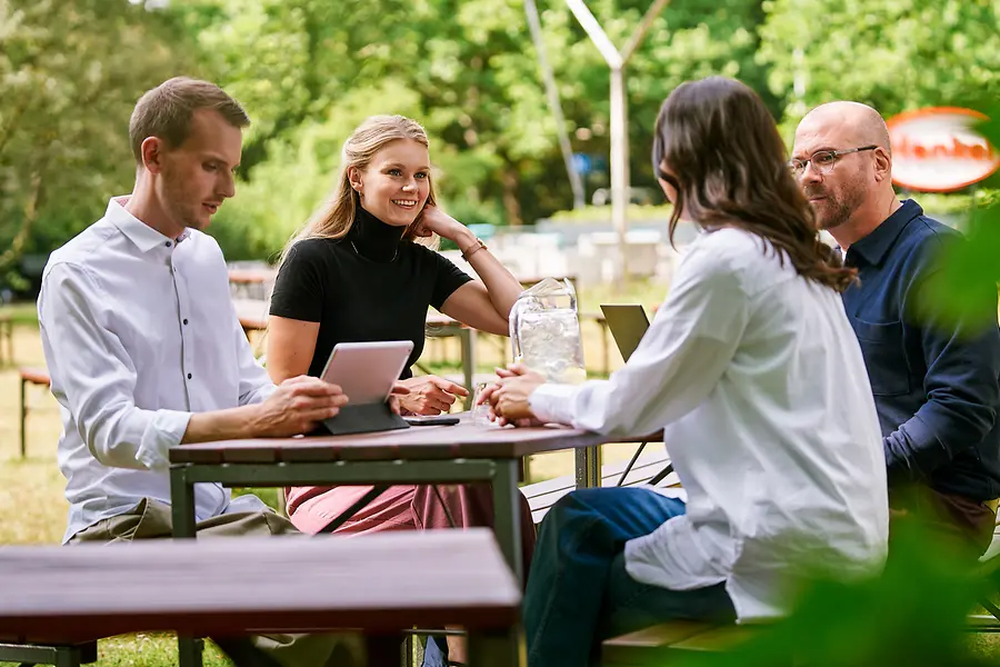 En grupp kollegor som sitter tillsammans utomhus och diskuterar arbetet med surfplattor och bärbara datorer, vilket symboliserar samarbete och en öppen, teamorienterad kultur hos Henkel.