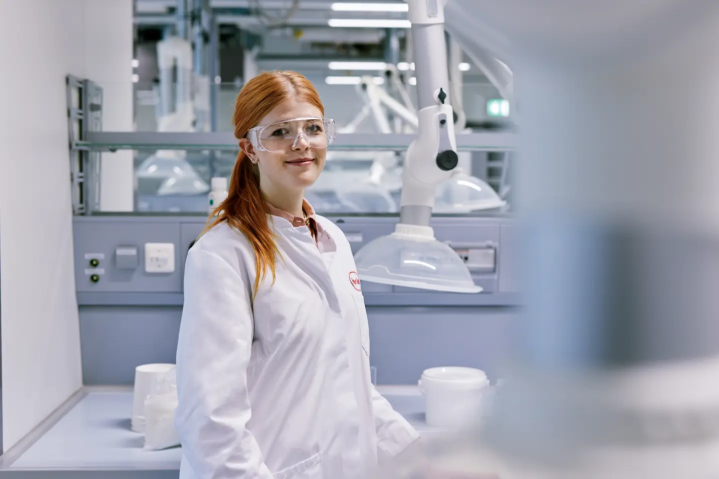 En nyutexaminerad som inleder sin karriär hos Henkel, klädd i en vit labbrock och stående i en modern laboratoriemiljö med teknisk utrustning i bakgrunden.